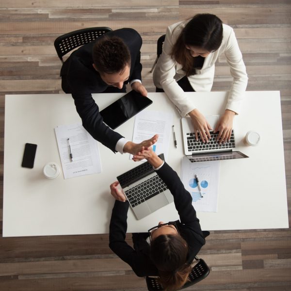 Top view of colleagues working together at laptops with handouts, coffee, devices around. Male worker giving high five to female associate during negotiations. Concept of success, teamwork, cooperation